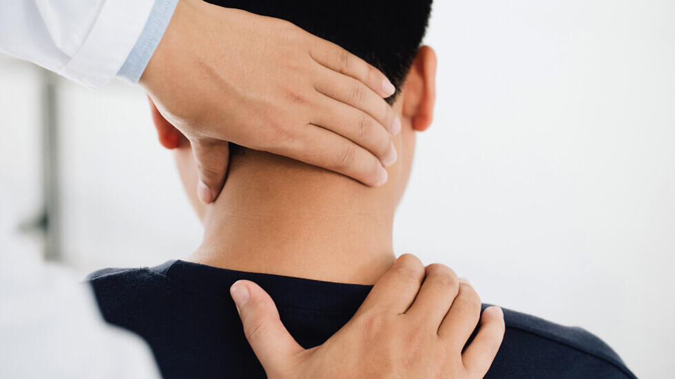 Physiotherapeut hält den Kopf eines Patienten und massiert dessen verspannte Nackenmuskulatur