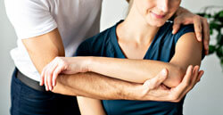 Physiotherapeut behandelt die Schulter und den Ellenbogen einer Patientin während der Krankengymnastik.