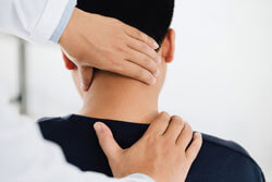 Physiotherapeut hält den Kopf eines Patienten und massiert dessen verspannte Nackenmuskulatur